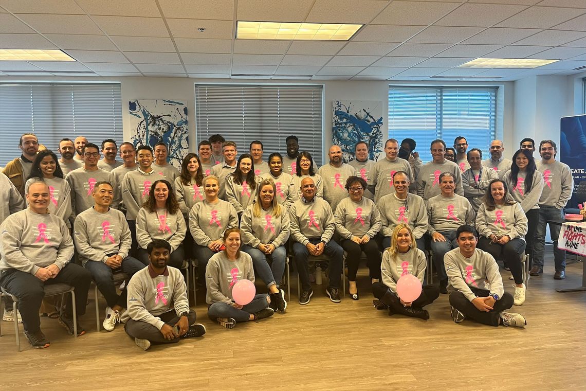 group of employees wearing breast cancer shirts, some holding pink balloons