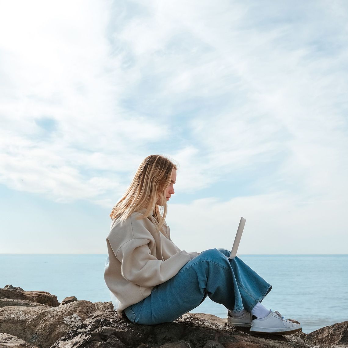 woman sitting on rocks by the water on her computer